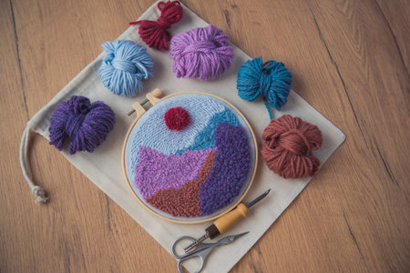 Embroidered mountains in a round frame with skeins os wool, punch needle and scissors around. Fiber...