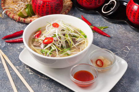 tasty Vietnamese Pho Bo with rice noodles and beef on a gray background