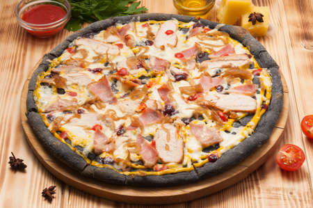 tasty pizza with chicken bacon and onions on black doughの写真素材
