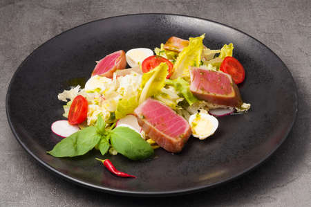 salad with fried tuna, vegetables and quail egg on a black plateの写真素材