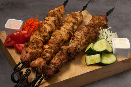 assorted kebabs on metal skewers with vegetables and saucesの写真素材
