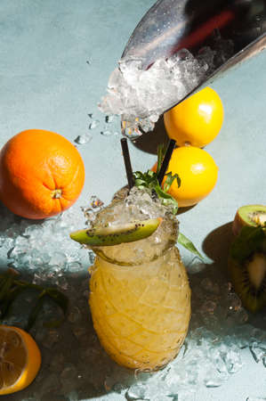 tasty yellow cocktail with crushed ice decorated with orange, lemon and kiwiの写真素材