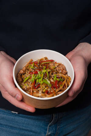 a man holds a bowl of tasty udon noodles with chicken and vegetablesの写真素材