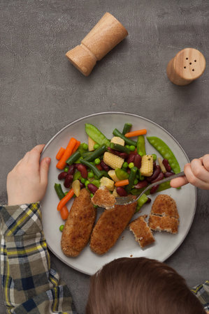 the child eats tasty cutlets with vegetables. top view