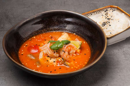 tasty tom yam with seafood in a dark dish and riceの写真素材