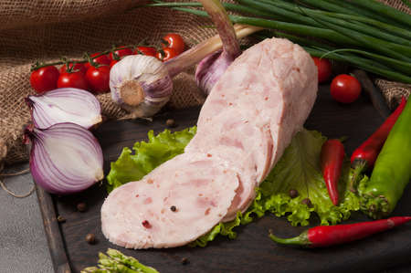 tasty chicken ham on a wooden board decorated with fresh vegetablesの写真素材