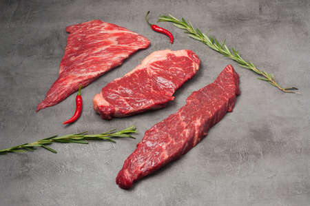 a mix of fresh marbled beef steaks garnished with rosemary and chili pepper. horizontal photoの写真素材