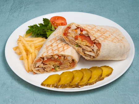 tasty shawarma with chicken and vegetables, French fries and pickled cucumber on a blue backgroundの写真素材