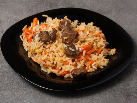 tasty traditional Uzbek pilaf on a black plate on a gray background