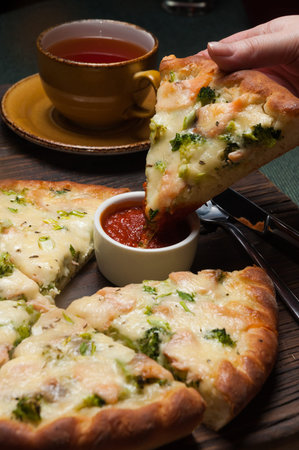 girl dips a slice of tasty pizza with salmon and broccoli in tomato sauce
