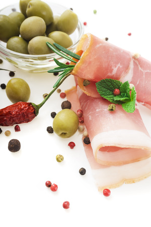 Sliced prosciutto with rosemary and olives on white backgroundの写真素材