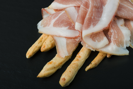 Grissini bread sticks with prosciutto on a blackの写真素材