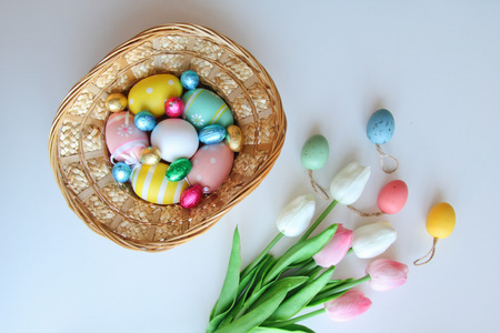 Easter festive frame with eggs in a basket and tulips on white wooden tableの写真素材