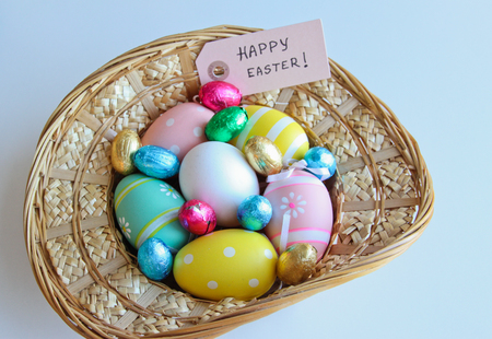 Easter festive frame with eggs in a basket and on white wooden table with Happy Easter card.の写真素材