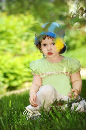 Portrait of a beautiful little girl in a summer park on a green grassの写真素材