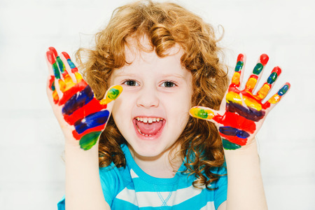 Happy little curly girl with hands in the paint on a light background.の写真素材