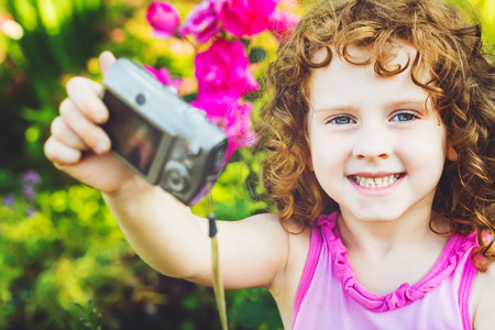 Happy little girl taking self photo on a summer garden.の写真素材