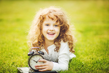 Girl lying on the grass and holding alarm clock.の写真素材