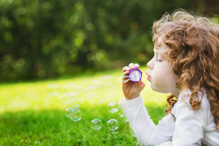little girl blowing soap bubbles, closeup portrait beautiful curly babyの写真素材