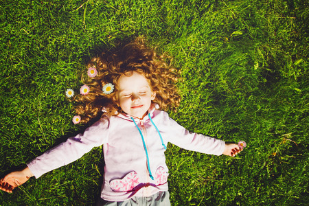 Curly girl lies on the grass and smiling, toning photo.の写真素材