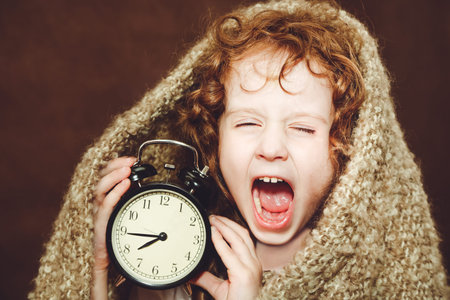 Curly girl  yawn and holding alarm clock. Photo toned brown.