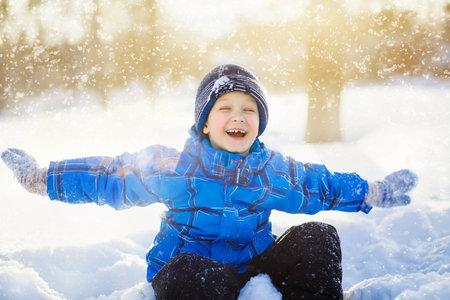 Laughing little boy, sitting in the snow park.の写真素材
