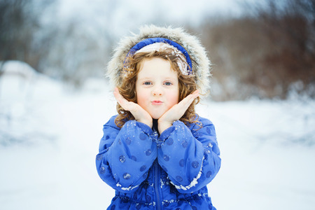 Happy little girl sends a kiss, playing in the snow park.の写真素材