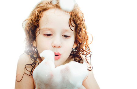 Happy little girl blowing foam with her hand isolated on white background.の写真素材