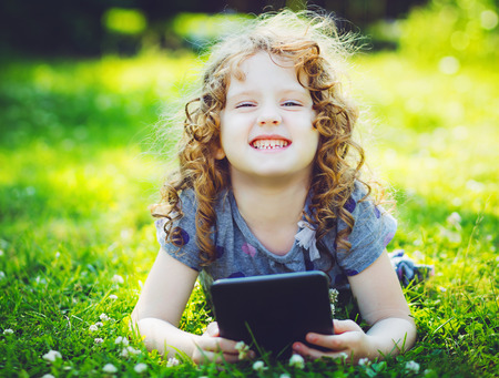 Little girl sitting on grass and playing tablet pcの写真素材