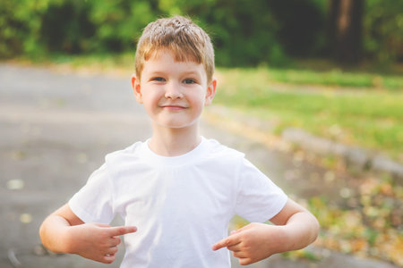 Happy little boy  pointing his fingers on a blank t-shirt, a place for your advertising. Childhood...