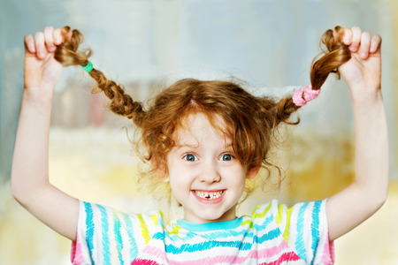 Laughing girl pull her pigtails up by hand and show her teeths. Childhood concept.の写真素材