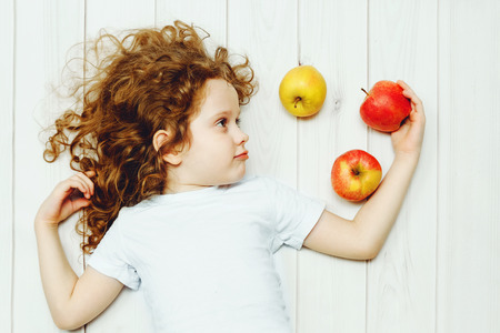 Happy child with red apples on light wooden floor. Top view.の写真素材
