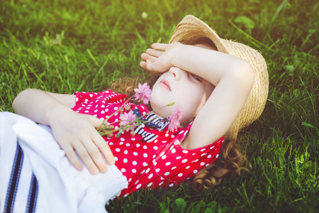 Offended little girl lies in the green grass and closed hands her face.の写真素材