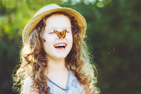Laughing curly girl with a butterfly on his hand. Happy childhood concept. の写真素材