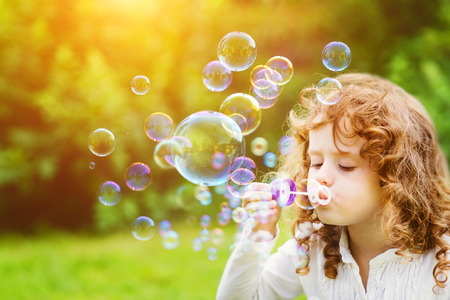 A little girl blowing soap bubbles in summer park. Background toninf for instagram filter.の写真素材