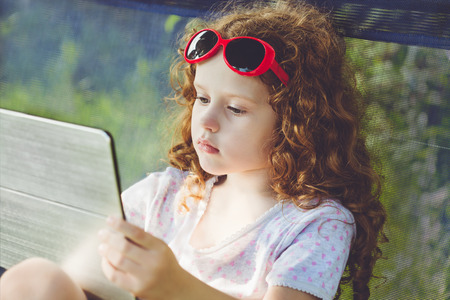 Serious little girl, playing tablet pc outdoors.の写真素材