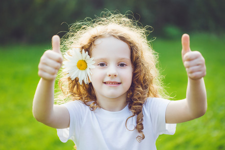 Laughing girl with daisy in her hairs, showing thumbs up.の写真素材