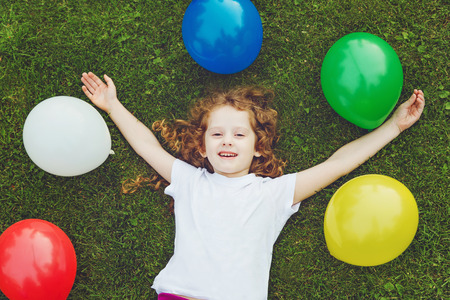 Happy child lies on green grass with rainbow balloons at summer park. Happy childhood, birthday party concept.の写真素材