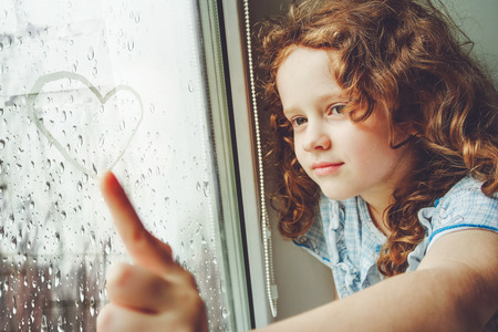 Happy child drawing heart on the window. Toning photo for instagram filter.の写真素材