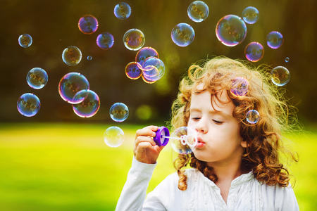 little girl blowing soap bubbles in summer park. Background toninf for instagram filter.の販売画像