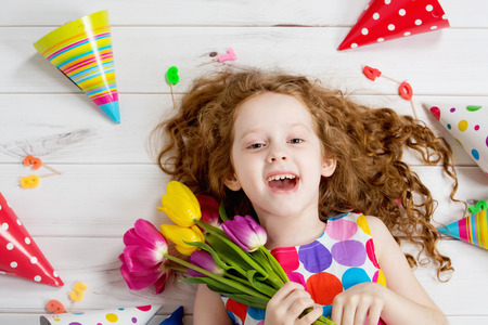 Happy laughing girl in birthday party lying on wooden floor.の写真素材