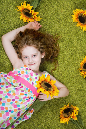 Curly girl with sunflower in grass carpet.の写真素材