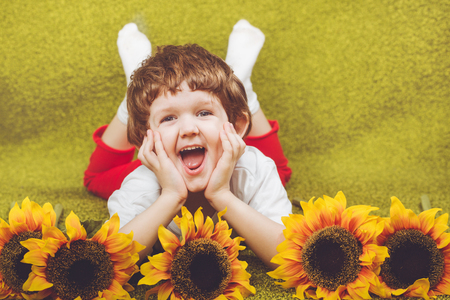 Cute child with sunflower lying on the green carpet.の写真素材