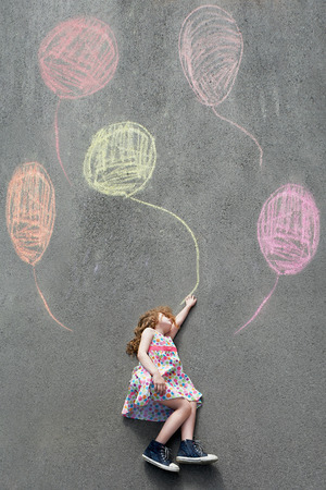 Dreamy little girl l flying with painted balloons. Happy childhood concept.の写真素材