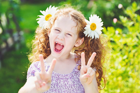 Little girl with daisy in her hair showing peace or victory hand triumph.