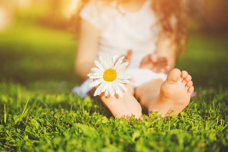 Child feet with daisy flower on green grass in a summer park.の写真素材