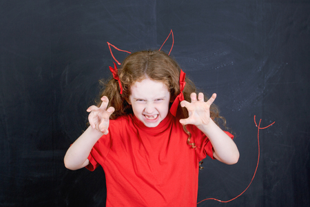 Angry girl in red t-shirt stand near horns and devil tail handdrawing on blackboard. Child character. Health and medical concept.の写真素材