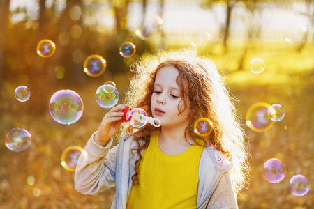 A little girl blowing soap bubbles in autumn park. Background toninf for filter.