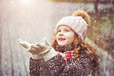 Cute little girl stretches her hand to catch falling snowflakes.の写真素材