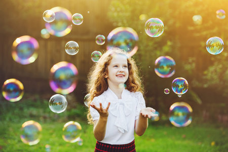 Beautiful child enjoying blowing soap bubbles in the summer on nature. Background toning instagram...